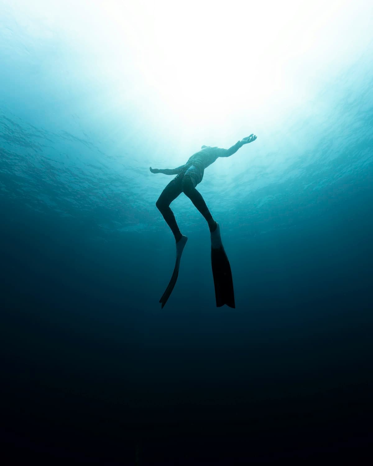 A diver finning down into darkening blue, light fading behind