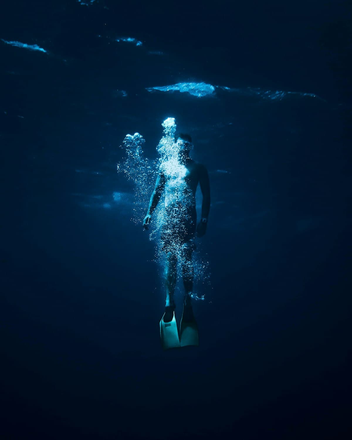 A diver descending into dark water, trailing a thin stream of bubbles