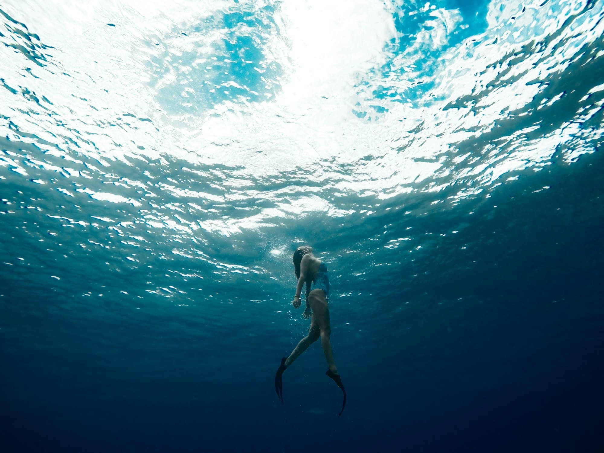 A freediver rising toward the bright, rippled underside of the surface